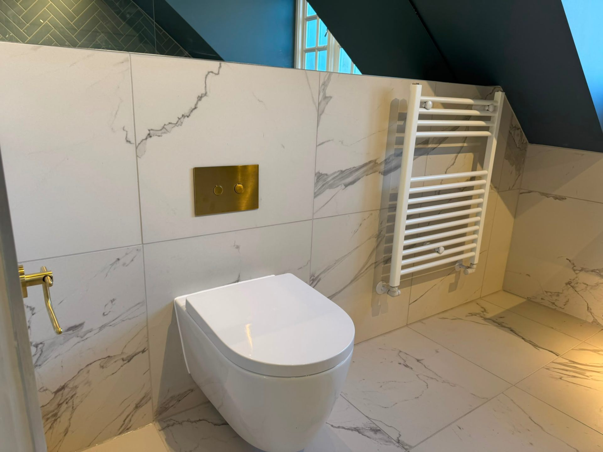 Wall-hung WC and heated towel rail in a marble-effect loft bathroom by Heat Solution London