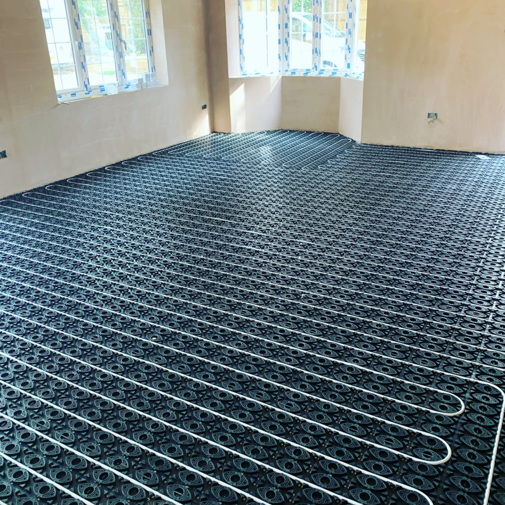 Underfloor heating manifold and pipe grid installed across a plastered new-build room in Ashford