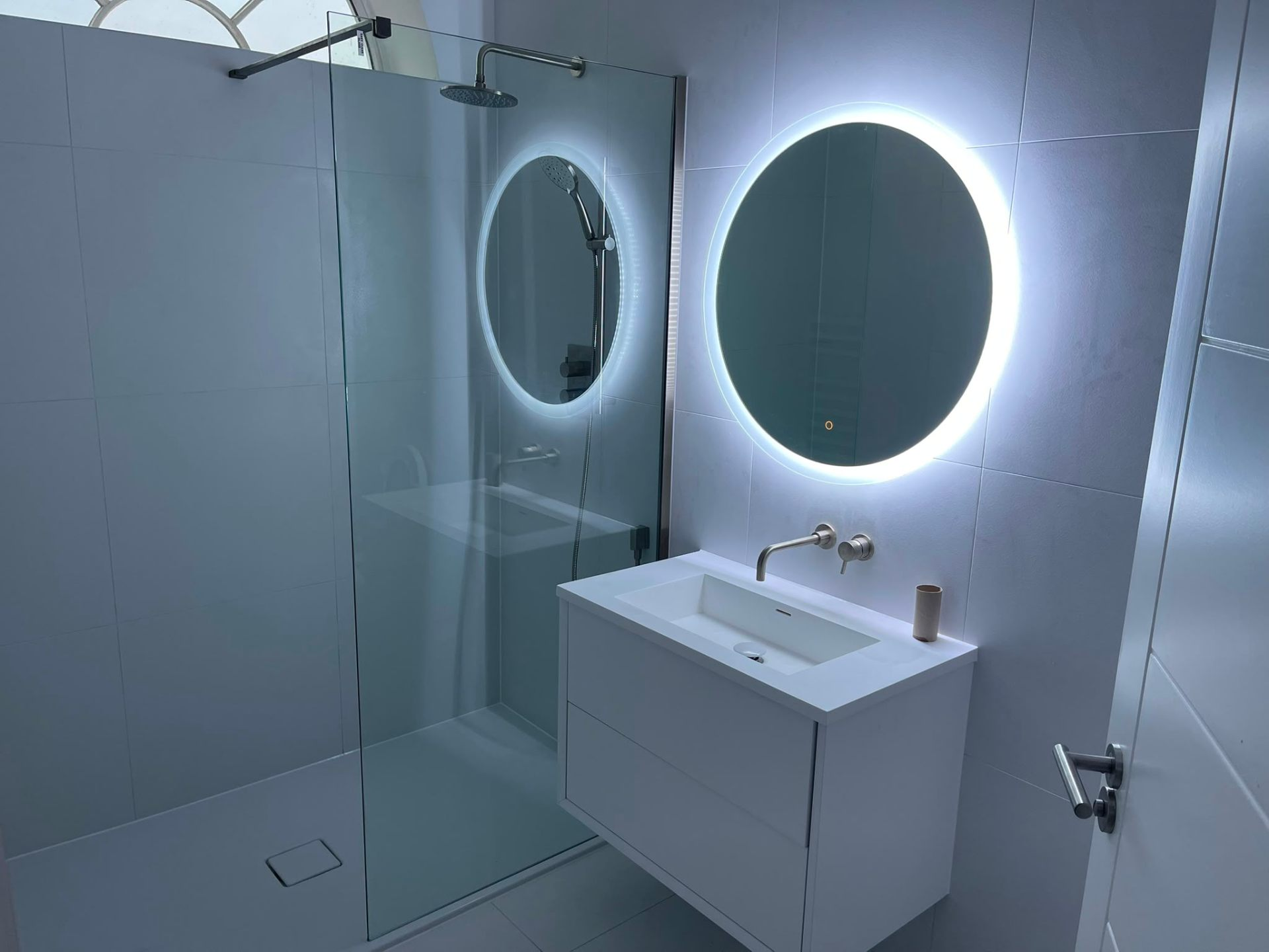 Modern white bathroom with walk-in shower, backlit round mirror and floating vanity by Heat Solution London