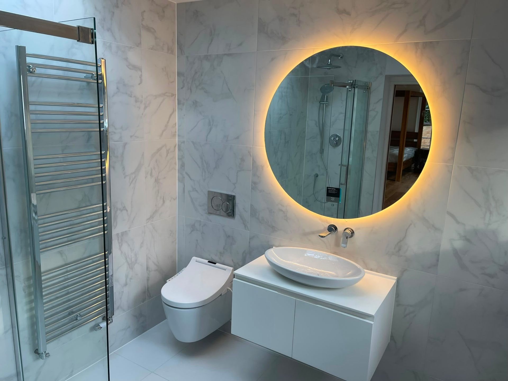 Marble-tiled loft bathroom installation with wall-hung vanity and heated towel rail by Heat Solution London, Surrey